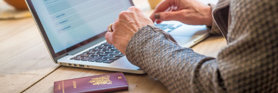 Persoon achter een laptop waarbij een paspoort op het bureau ligt.