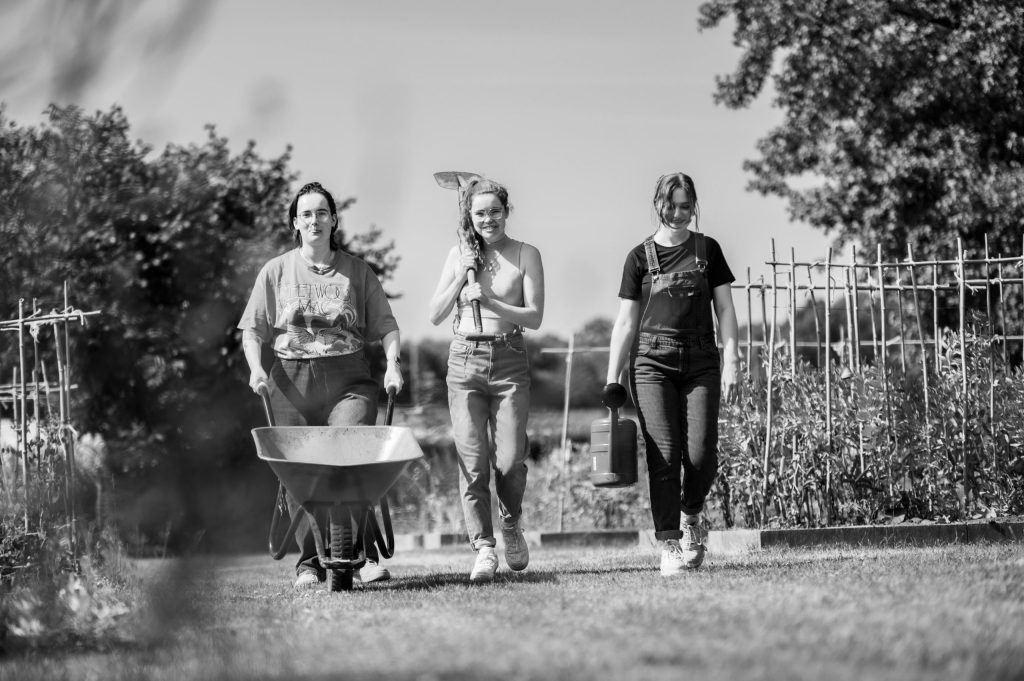 Drie jongeren wandelen door tuin met tuingereedschap