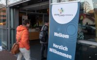 Mensen die naar binnen lopen bij de Grenslandcoferentie. Er staat een bord 'Welkom bij de Grenslandconferentie'.