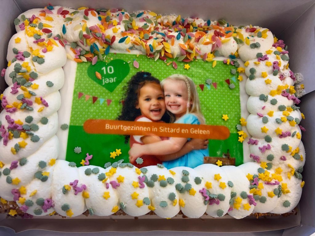 Slagroom taart met foto van 2 vrolijke meisjes en de tekst 10 jaar buurtgezinnen in Sittard en Geleen